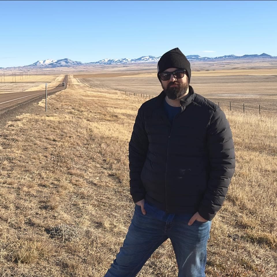 Scott on the highway shoulder in Montana, mountains behind